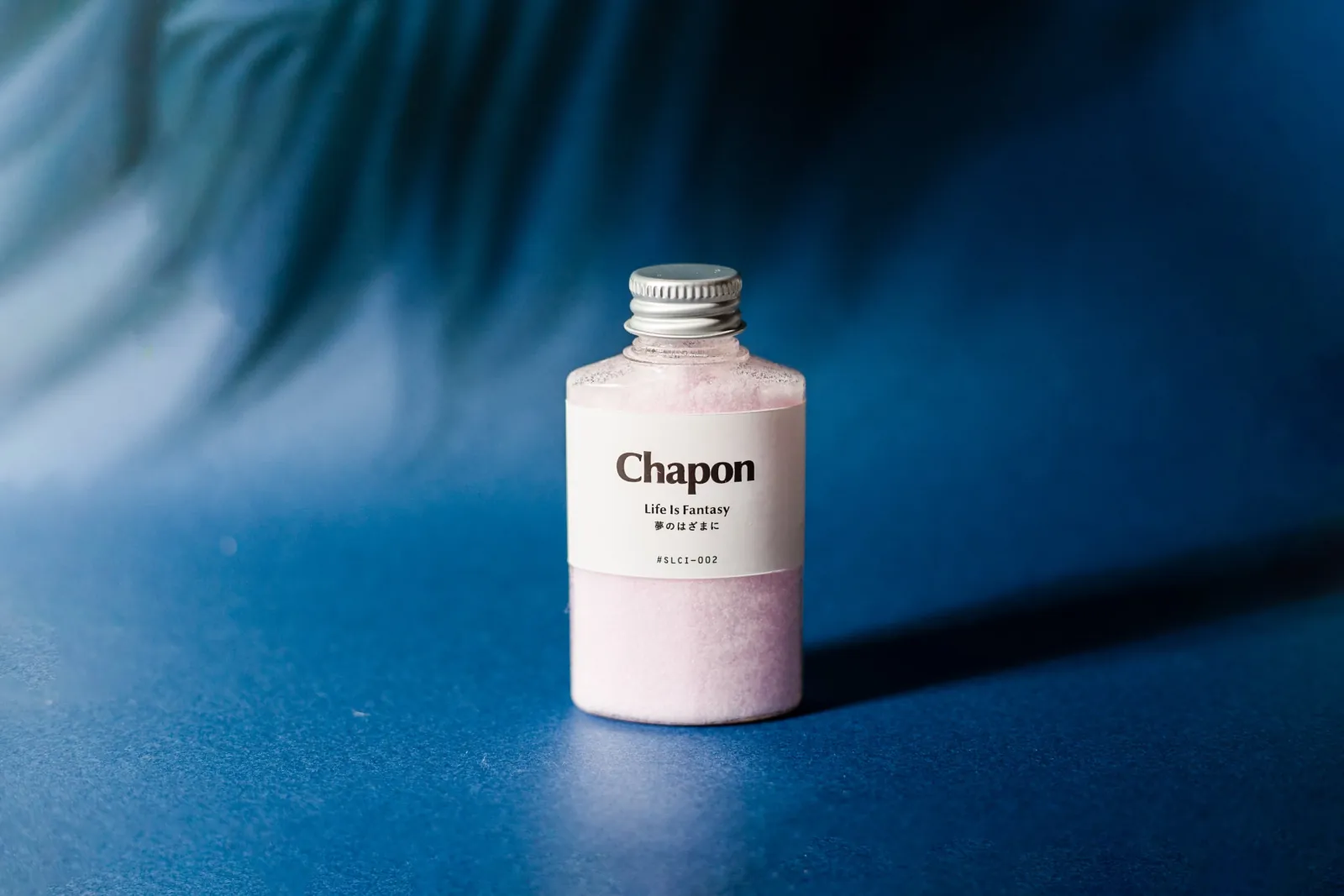 青い背景に置かれたピンク色のChapon入浴剤ボトルと葉の影